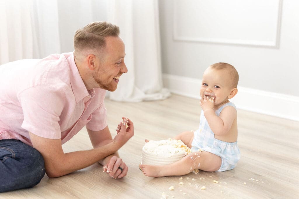 family photographer Louisville KY father laughing with baby during cake smash birthday session on studio floor