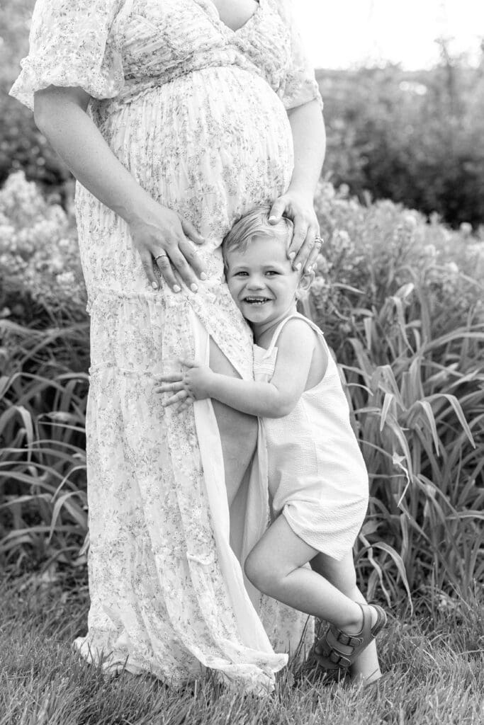 Louisville KY maternity photographer capturing toddler hugging mother’s baby bump during outdoor maternity session
