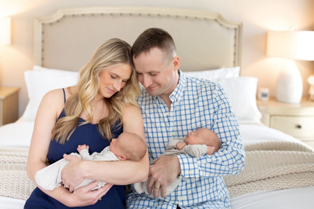 
lifestyle newborn photography Louisville KY mother and father sitting on bed holding twin newborn babies in home bedroom session