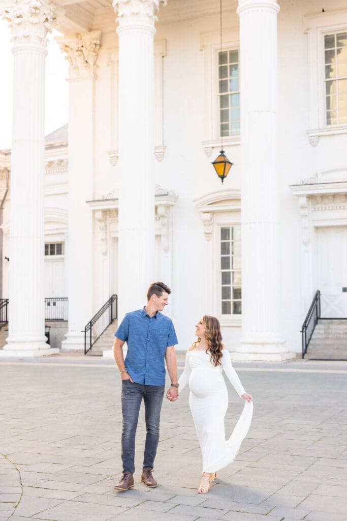 Maternity photographer in Louisville Kentucky captures couple holding hands at golden hour beside the Louisville Water Tower columns