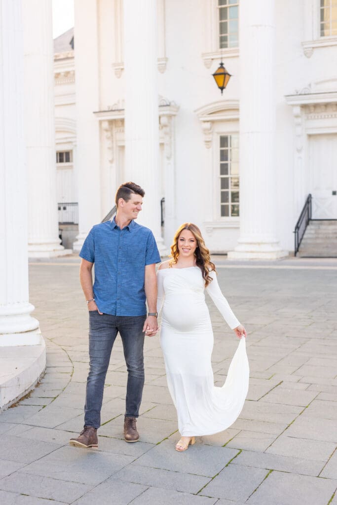 Louisville maternity photographer captures expectant couple walking among white Greek Revival columns at the Louisville Water Tower