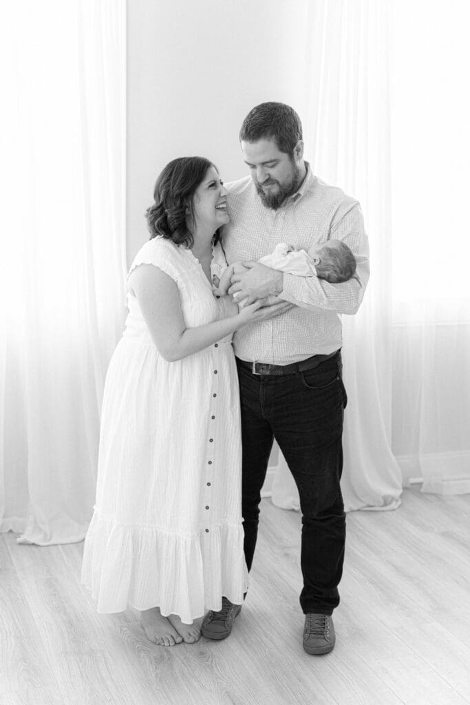 lifestyle newborn photography Louisville KY mother and father holding newborn baby in bright white studio