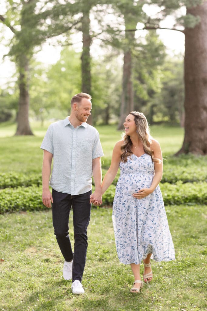 family maternity session Louisville KY pregnant mother in floral dress walking hand in hand with partner through tree lined park