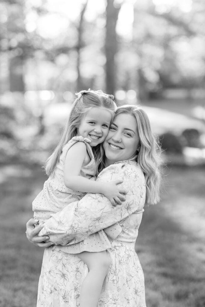 maternity photography Louisville KY black and white photo of older sister hugging and smiling with younger sister outdoors